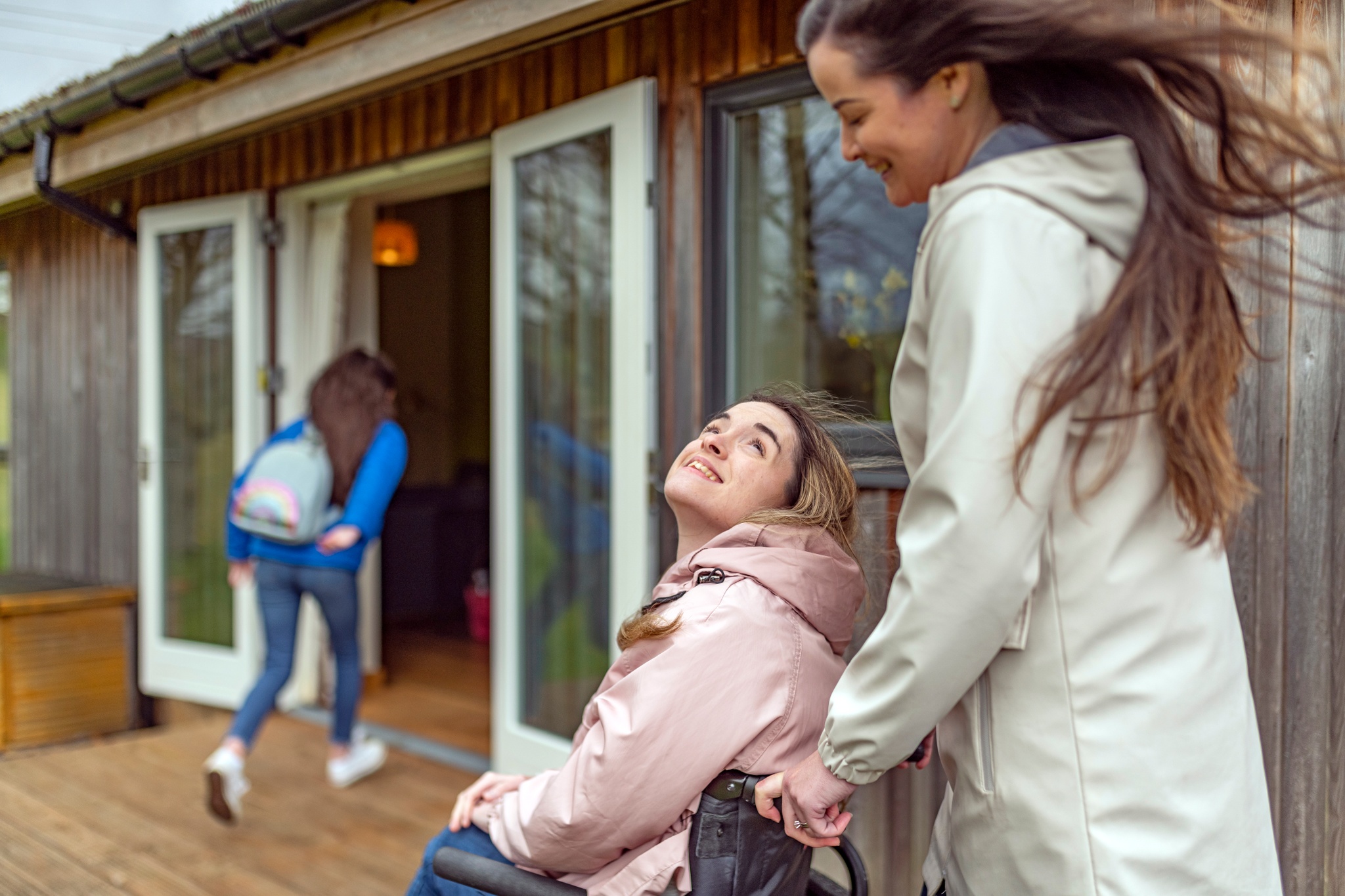 A women pushes a young woman in a wheelchair across the decking of the Green House which offers accessible accommodation for up to four people.