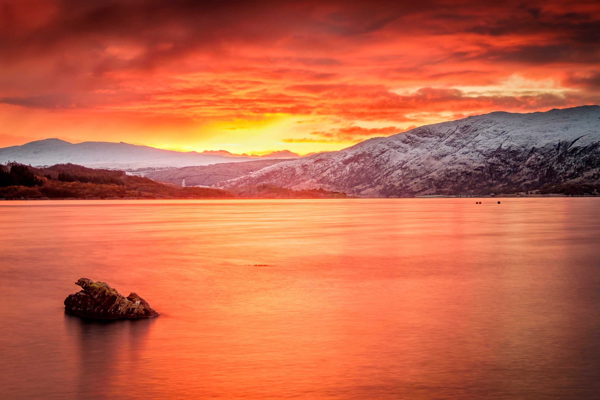 The light from a spectacular early winter sunrise over the first of the Winter's snow paints the sky and Loch Sunart with shades of red