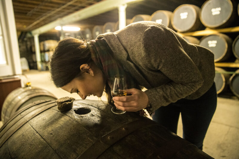 Glen Ord The Nearest Distillery To Inverness Loch Ness In The Highlands Of Scotland  Young Woman Smelling Whisky Through A Hole In An Oak Barrel